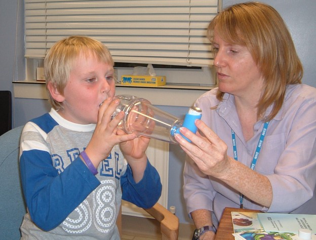 A healthcare professional helping a male child use their inhaler spacer with mouthpiece attachment