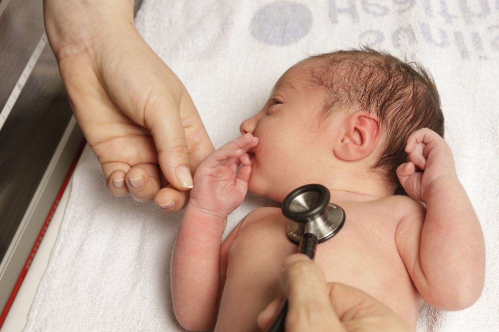 An image of a new born baby lying down on a hospital bed with a stethoscope on their chest.