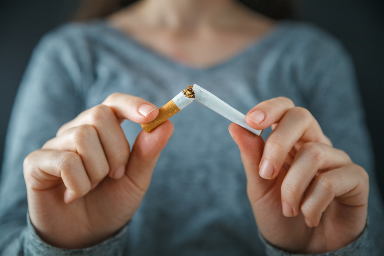 A close up image of two hands holding a cigarette. The cigarette has been broken in half so it is no longer smokable.