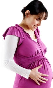 White, brunette female holding her pregnant belly and looking down.