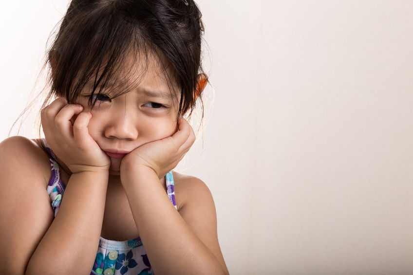 BAME, female child holding her face in her hands whilst looking sad or upset.