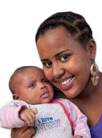 BAME female smiling and looking at the camera whilst holding her baby.