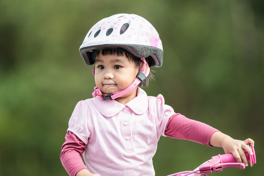 Female, BAME, young child wearing a pink bike helmet whilst sat on her bicycle.