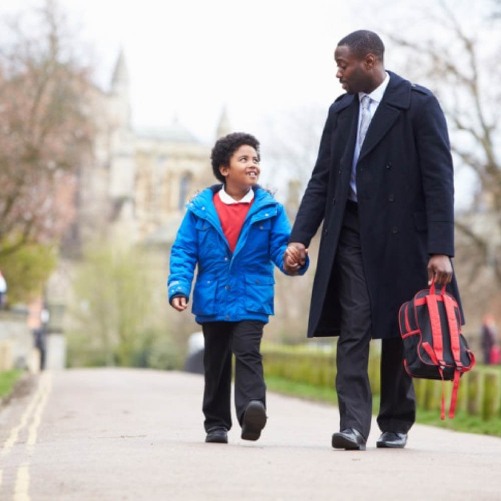 BAME father and his son holding hands walking outside together.