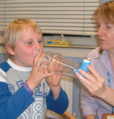 Young boy, around 8 years of age, using his inhaler and spacer with help from a female nurse.