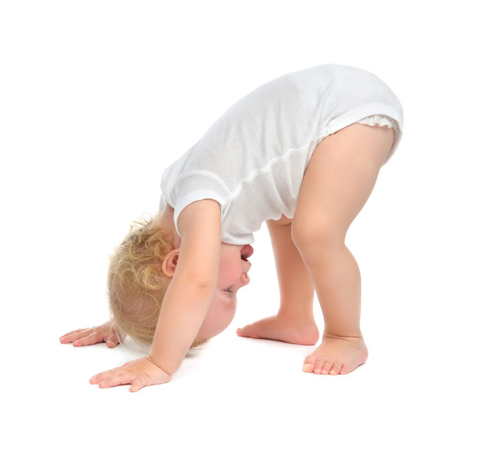 A baby bent over towards the ground, with their hands placed on the floor.