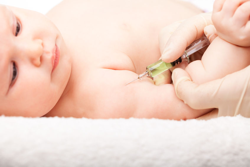 An image of a baby lying down, about to have a vaccine needle inserted into their arm.